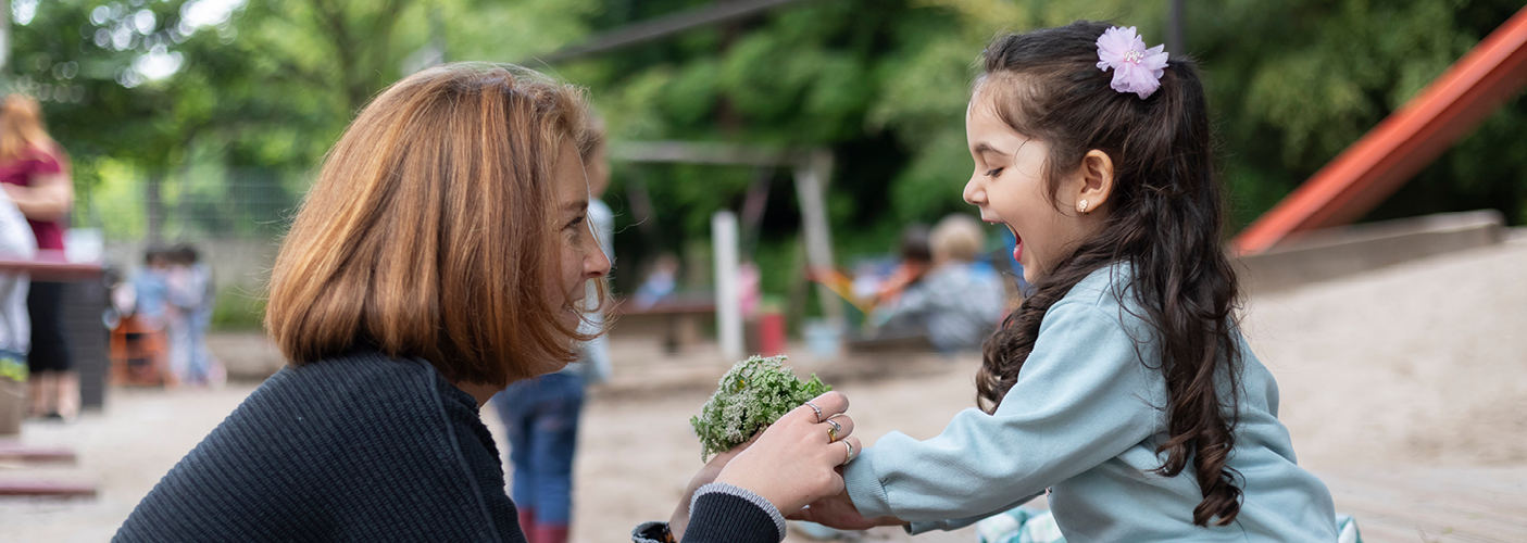 Eine erwachsene Person und ein Kind befinden sich auf Augenhöhe gegenüber. Eine erwachsene Person und ein Kind befinden sich auf Augenhöhe gegenüber.