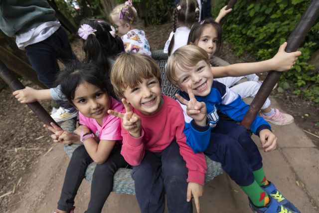 Mehrere Kinder sitzen auf einer Schaukel, zwei davon schauen lachend Richtung Kamera. Mehrere Kinder sitzen auf einer Schaukel, zwei davon schauen lachend Richtung Kamera.