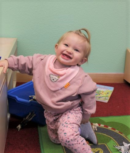 Ein Kind auf einer Spielmatte lacht Richtung Kamera.